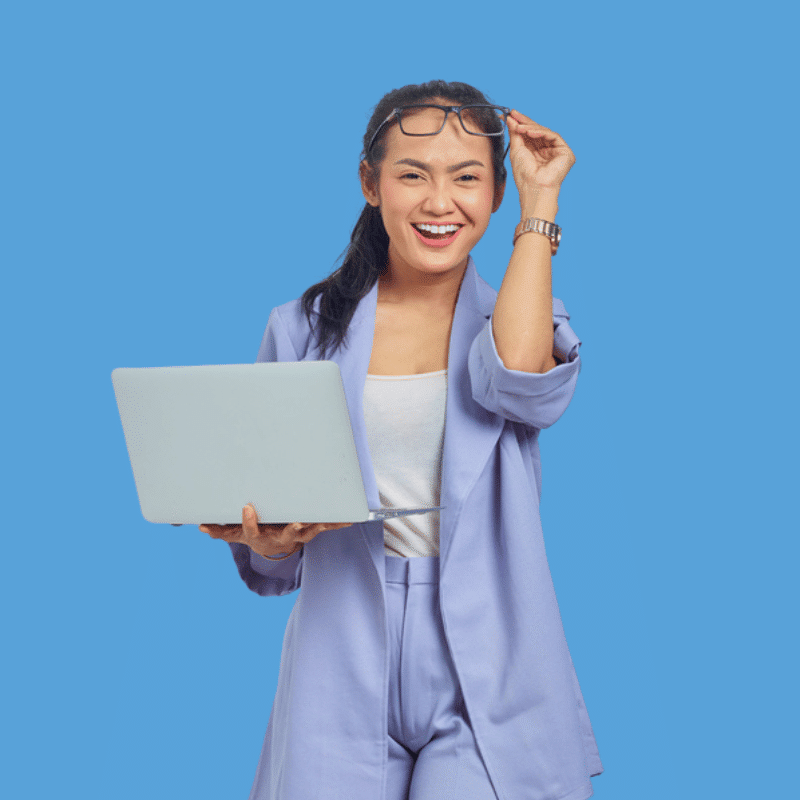 Frau vor blauem Hintergrund setzt sich Brille auf den Kopf, lächelt und hält Laptop in der anderen Hand